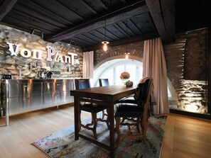 Un intérieur chaleureux avec un mur en pierre, une table en bois entourée de chaises et un coin bar doté d’un comptoir en acier inoxydable.