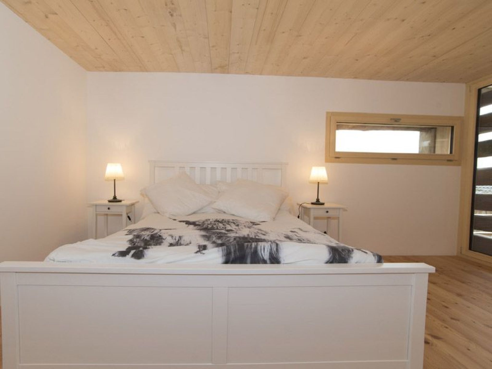 A bedroom with a bed, two bedside tables, a window, and a wooden ceiling.
