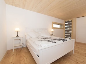 A white bed with a headboard, two bedside tables with lamps, and a wooden floor. - Haus La Grobla, (Donat), by Interhome (Lohn GR)