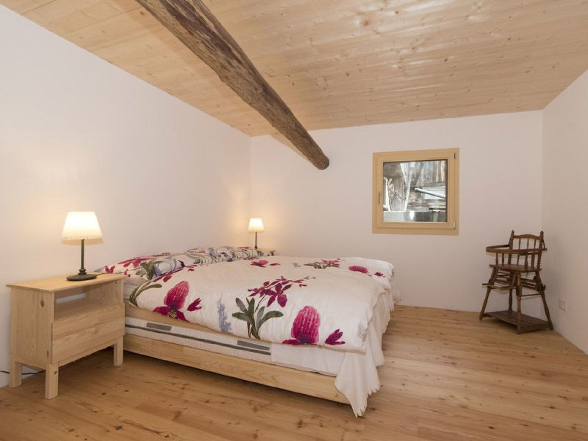Een slaapkamer met een houten bed, nachtlampjes, een houten stoel en een raam met uitzicht.