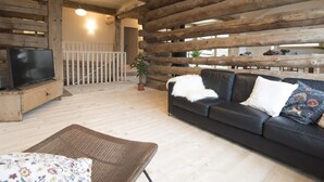 Ein Holzblockhaus-Interieur mit einer Couch, einem Fernseher, einem Korbsessel und einer Treppe.