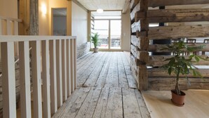 Ein Korridor mit Holzausbau, einer weißen Brüstung, einem Blumentopf und Blick ins Freie.