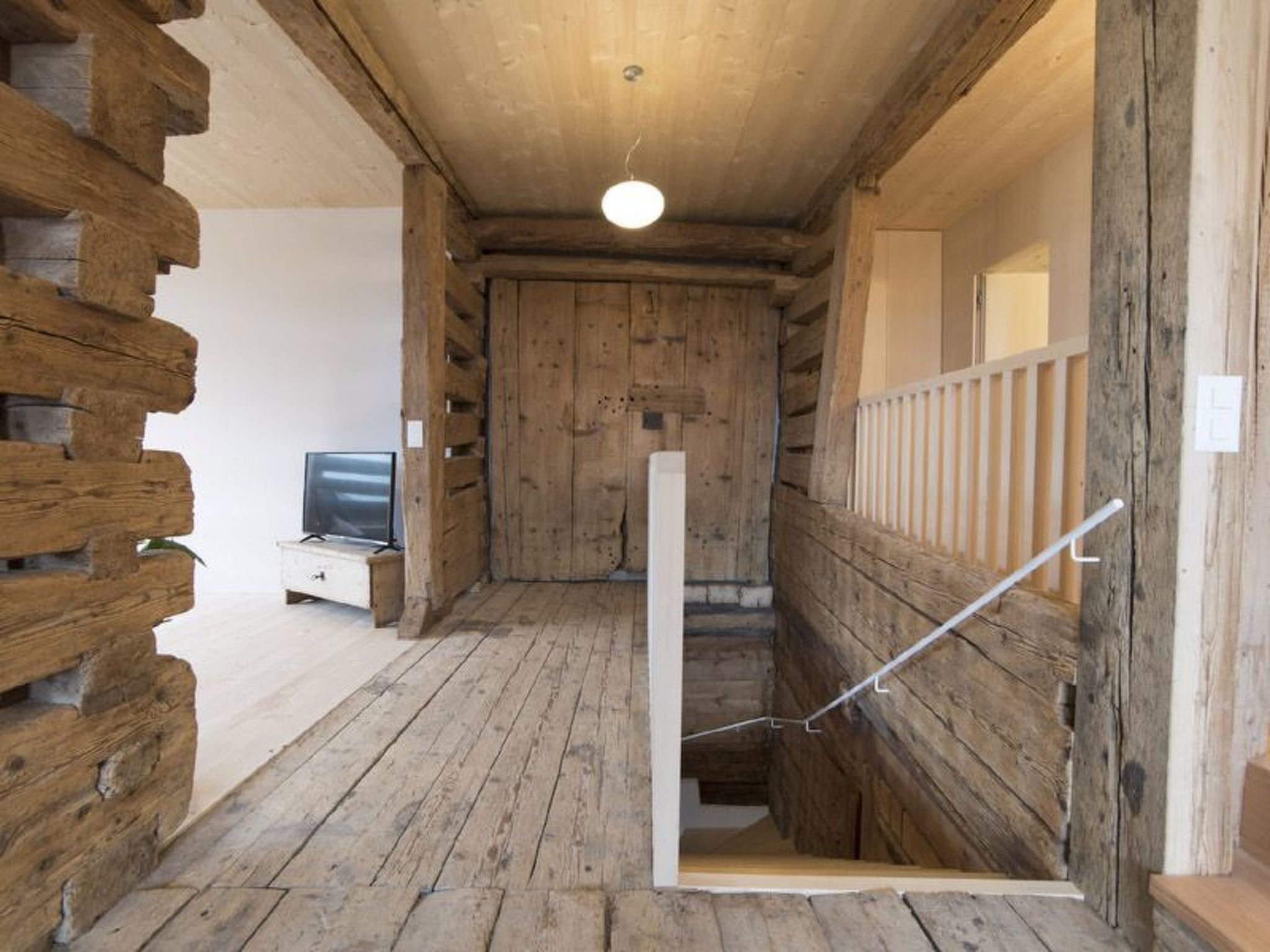 A wooden interior with a staircase, a television, and a white door.