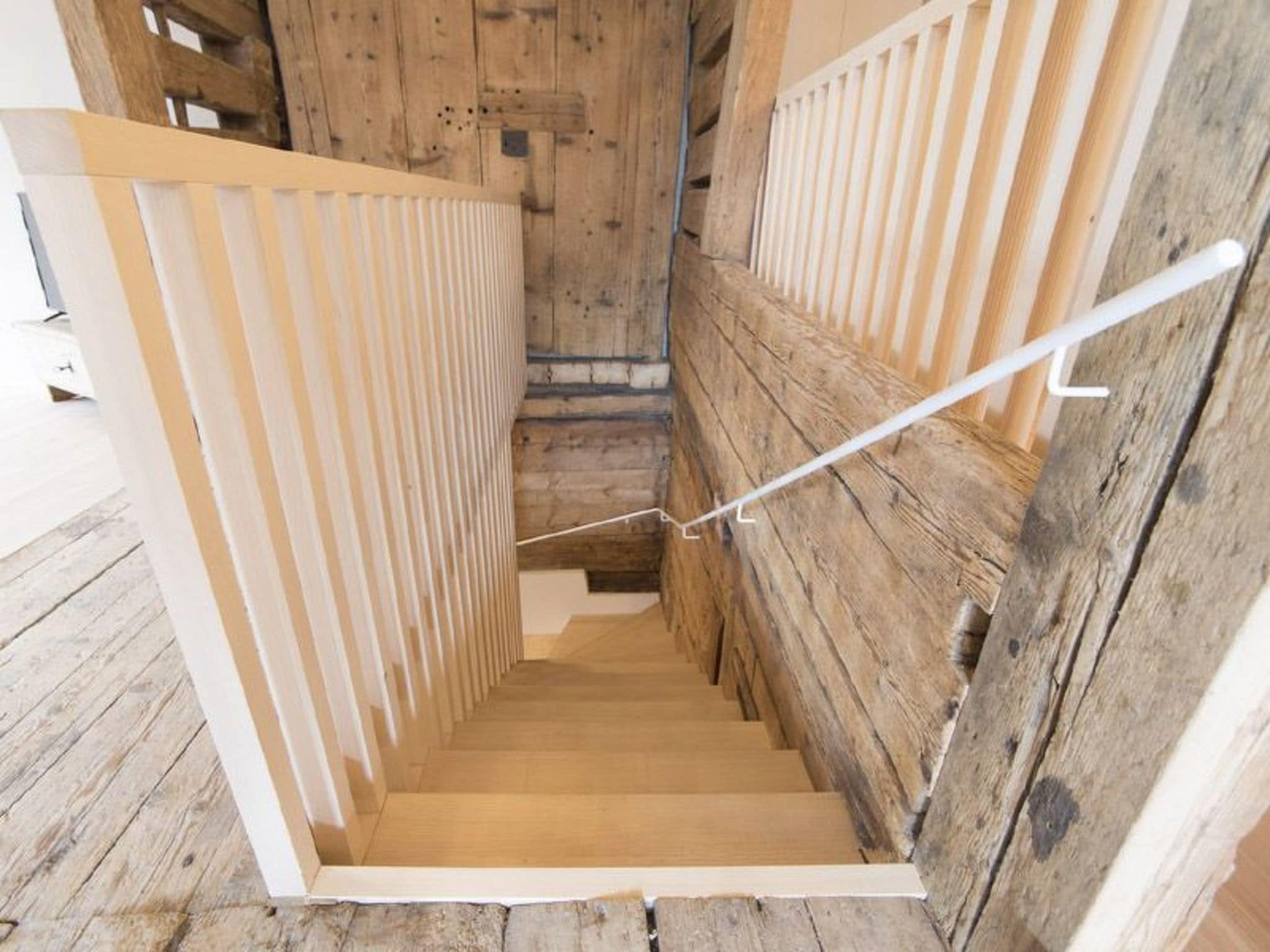 A wooden staircase with a white handrail and a wooden floor.