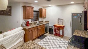 A compact kitchen with granite countertops, wooden cabinets, a refrigerator, and a checkered floor mat. - Amazing Retreat in Lehigh Acres Florida (Lehigh Acres)