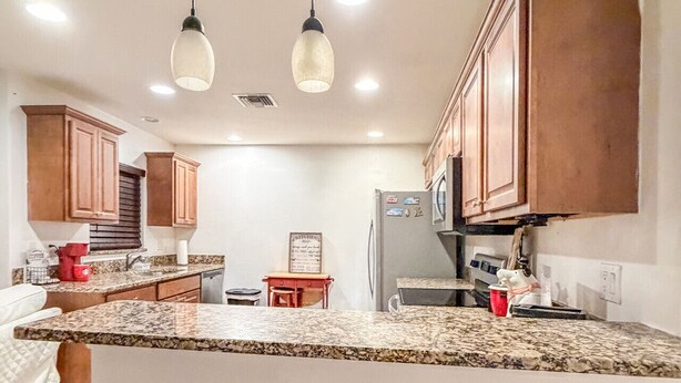 A kitchen with wooden cabinets, a granite countertop, and three red stools. - Amazing Retreat in Lehigh Acres Florida (Lehigh Acres)