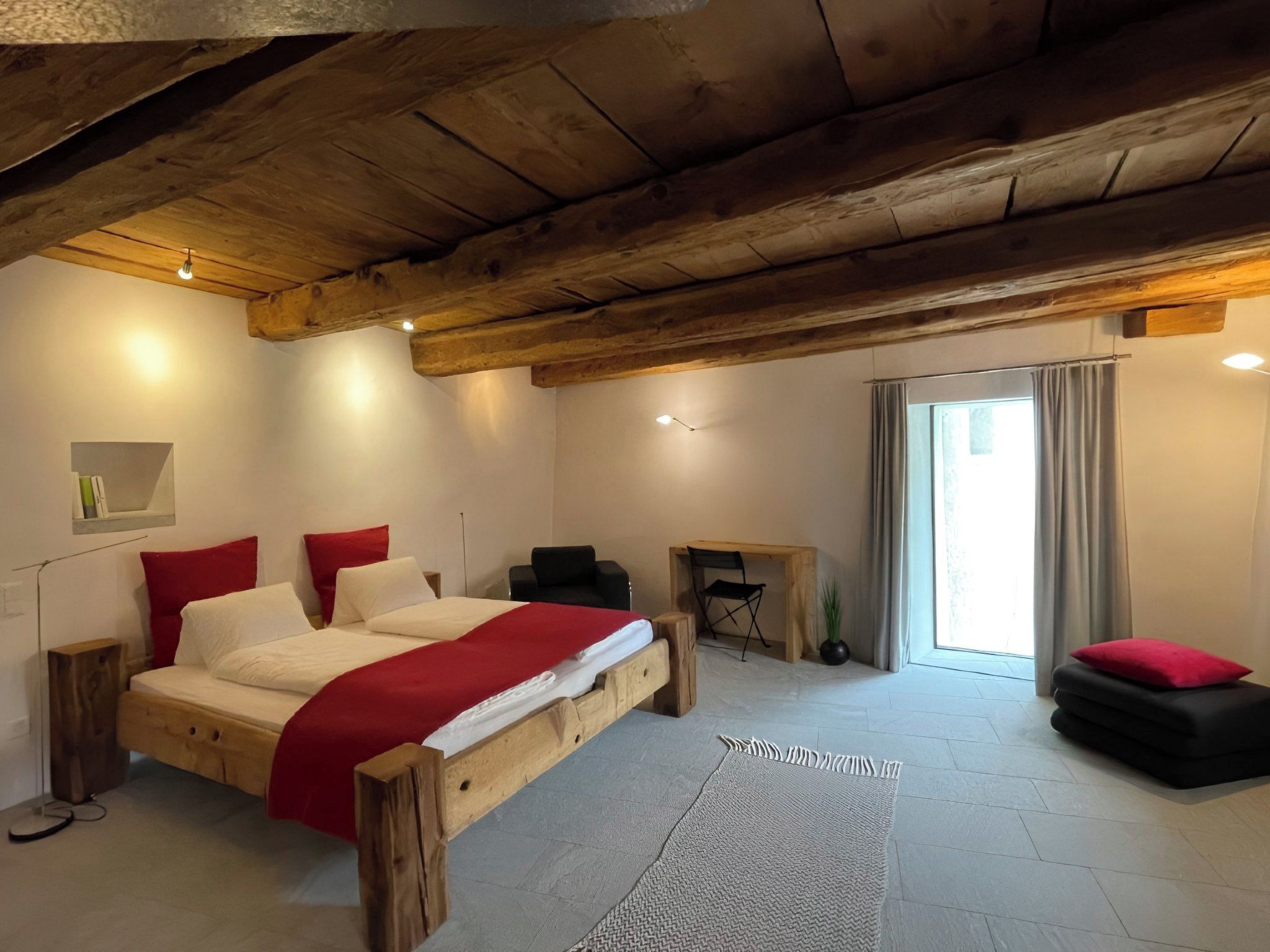 A bedroom with a wooden bed, a desk, a chair, and a window with curtains.