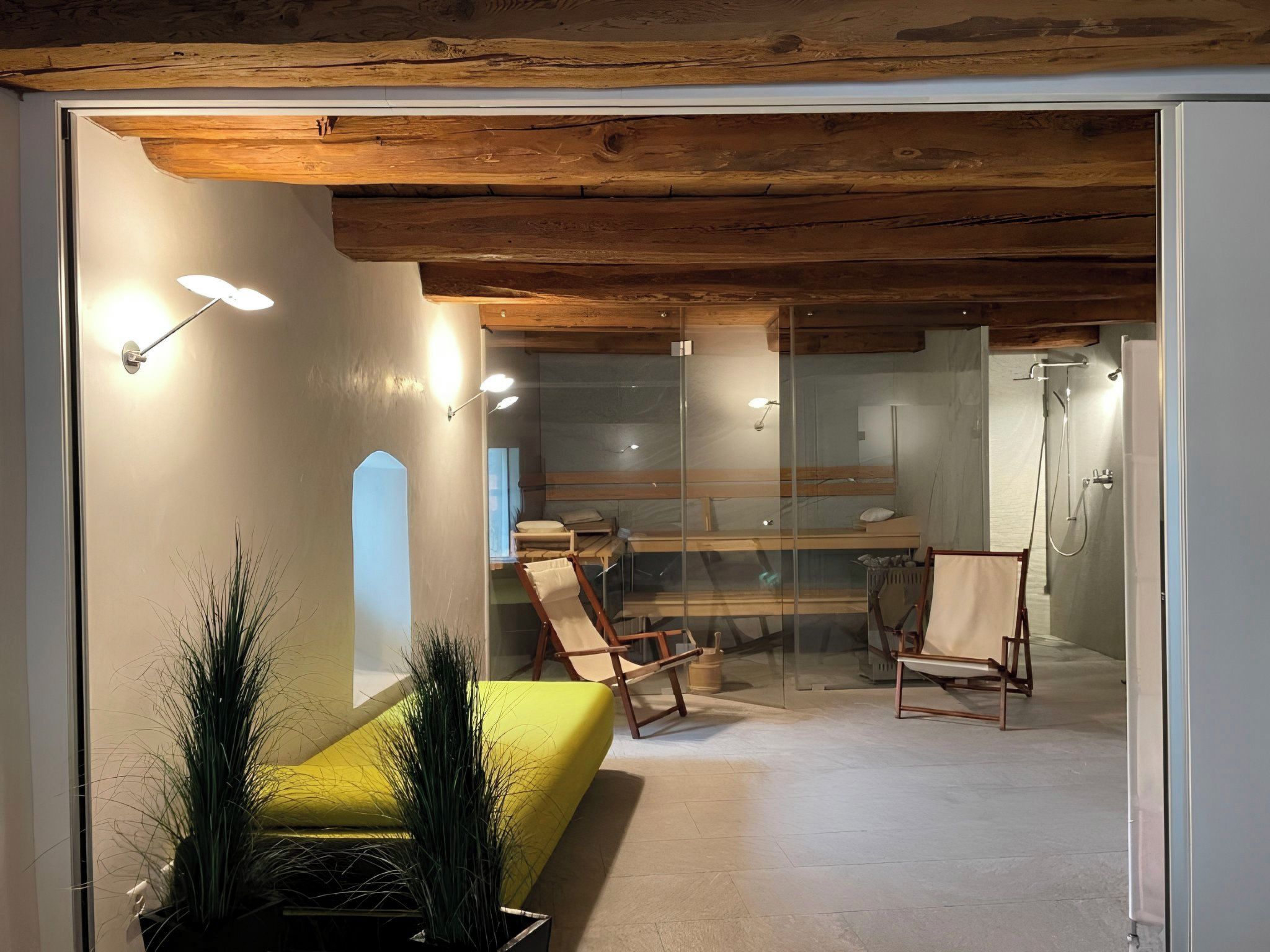 Ein modernes Interieur mit einer Glaskonstruktion, Holzbalken an der Decke und einer gelben Sitzbank.
