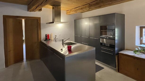 Une cuisine moderne dotée d’un îlot central, d’appareils électroménagers en acier inoxydable et de poutres en bois au plafond.