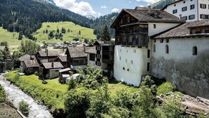 Un village traditionnel avec des bâtiments rustiques, une rivière et des montagnes en arrière-plan.