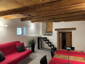 Ein gemütlicher Wohnbereich mit einem roten Sofa, einem kleinen Tisch, einer Topfpflanze, einer Treppe und einer Holzbalkendecke.