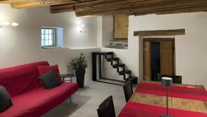 Un salon chaleureux avec un canapé rouge, une petite table et un escalier menant à un niveau supérieur.