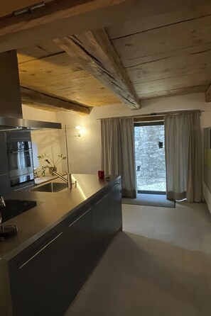 A modern kitchen with a central island, stainless steel appliances, and a view of a snowy landscape through a large window. - Historisches Teiler-Haus, (Splügen), by Interhome (Splügen)
