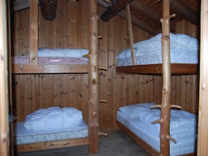 A wooden bunk bed room with two beds, each with a mattress and pillows.