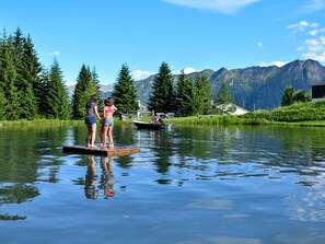 A lake with a wooden platform, two people standing on it, and a boat in the background.