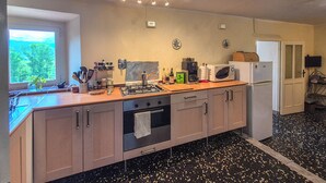 Cocina equipada con estufa, horno, microondas y refrigerador. Se ve un ventanal con vistas a zonas verdes.