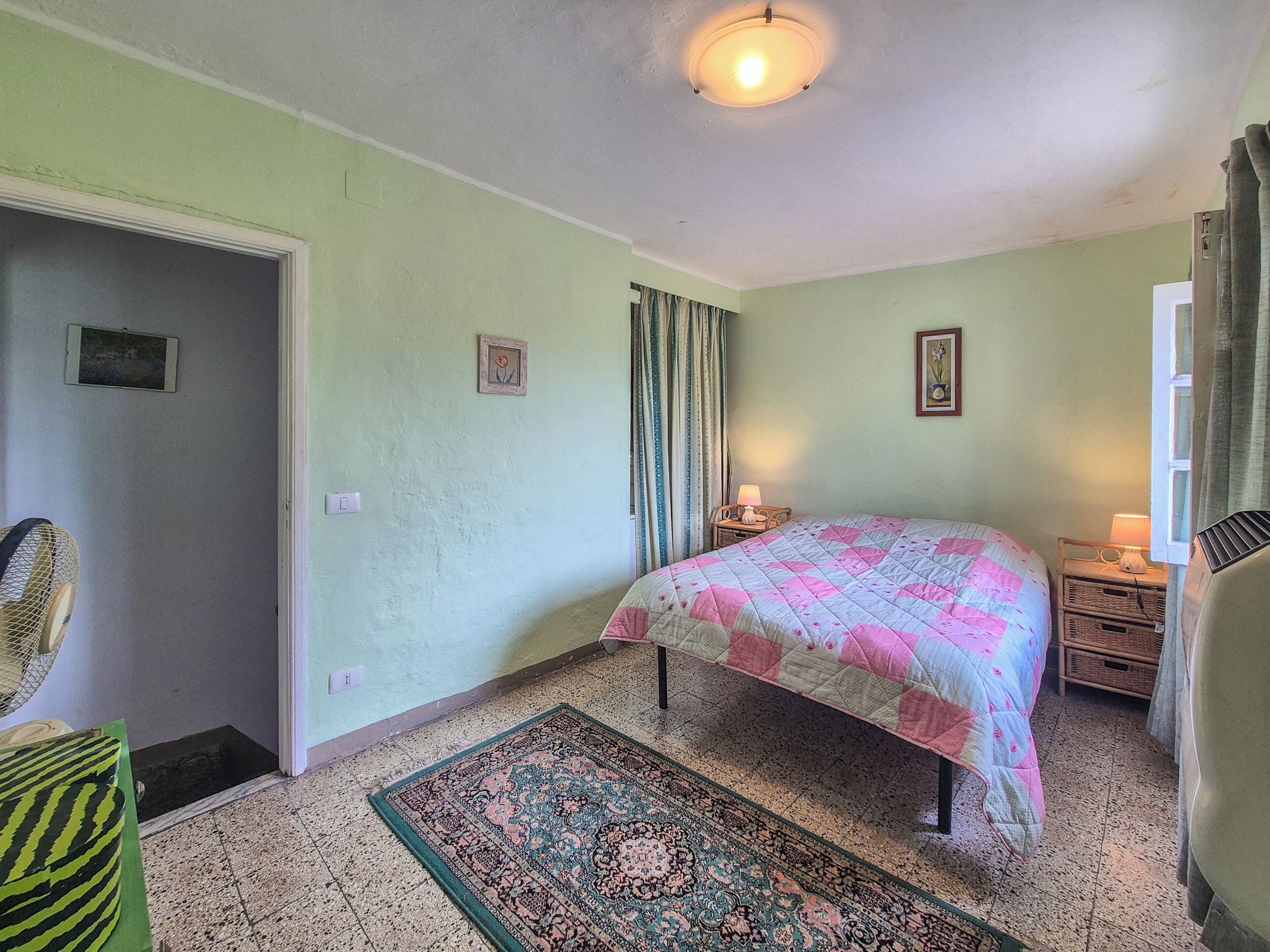 Une chambre à coucher avec un lit, un tapis, une table de chevet, une chaise et une porte.