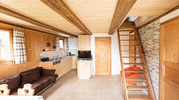 A wooden interior with a kitchen, a sofa, a TV, and a staircase.