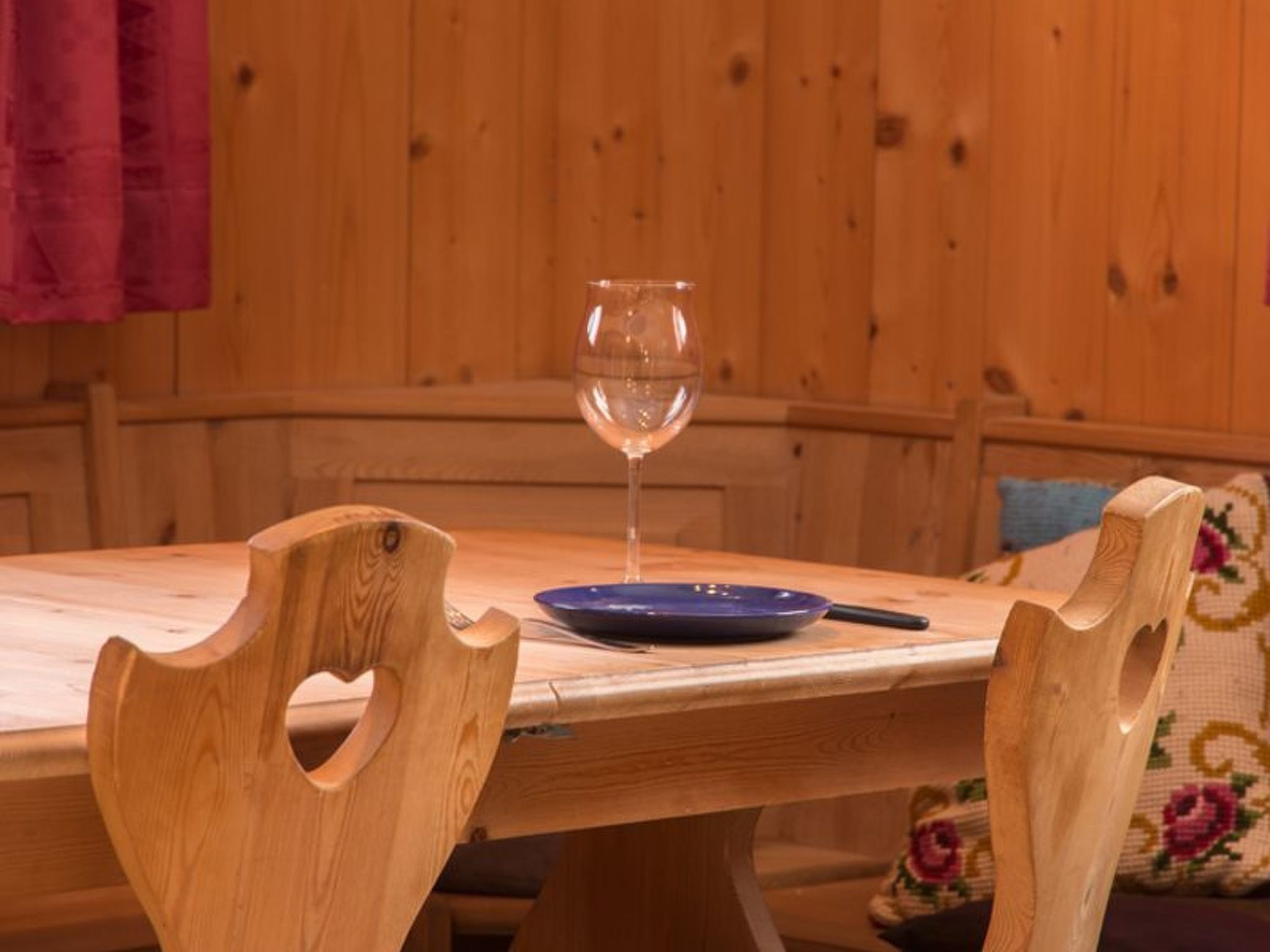 A wooden dining table with a wine glass and a blue plate, surrounded by wooden chairs.