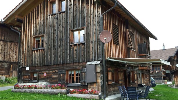 A rustic wooden building with a balcony, outdoor seating, and a satellite dish.