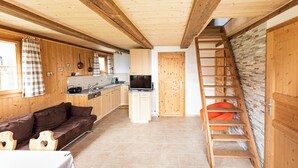 A cabin interior with wooden walls, a kitchen, a sofa, a dining table, and a staircase.