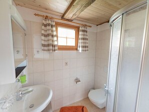 A bathroom with a shower, toilet, and sink. There is a window with curtains and a mirror above the sink.