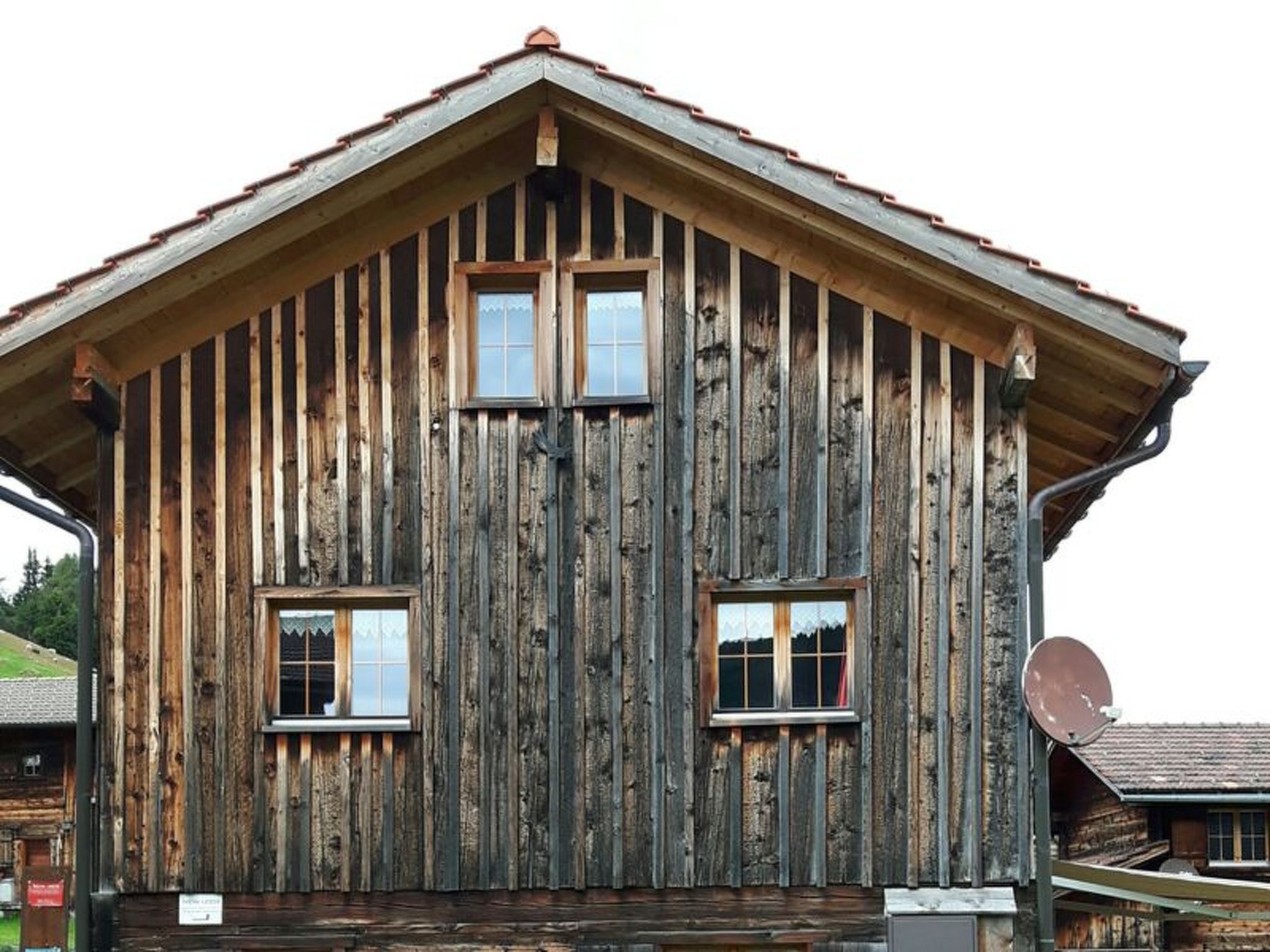 Un edificio rústico de madera con techo a dos aguas, dos ventanas y una antena parabólica.