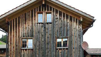 A rustic wooden building with a gabled roof, two windows, and a satellite dish.