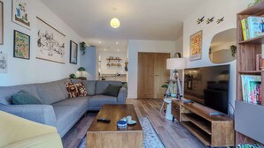 A modern living room with a grey sofa, a wooden coffee table, a TV, and a bookshelf. - Host & Stay | Austin House (Norwich)