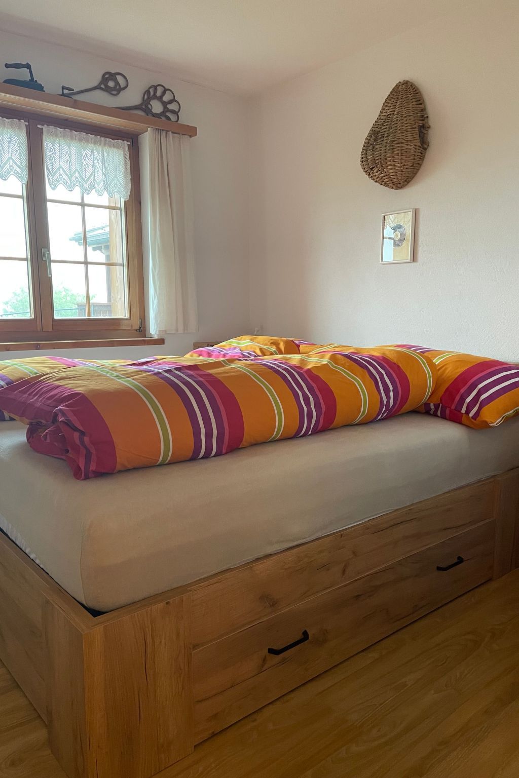 Una cama con una manta a rayas, una ventana con cortinas y un adorno en la pared.