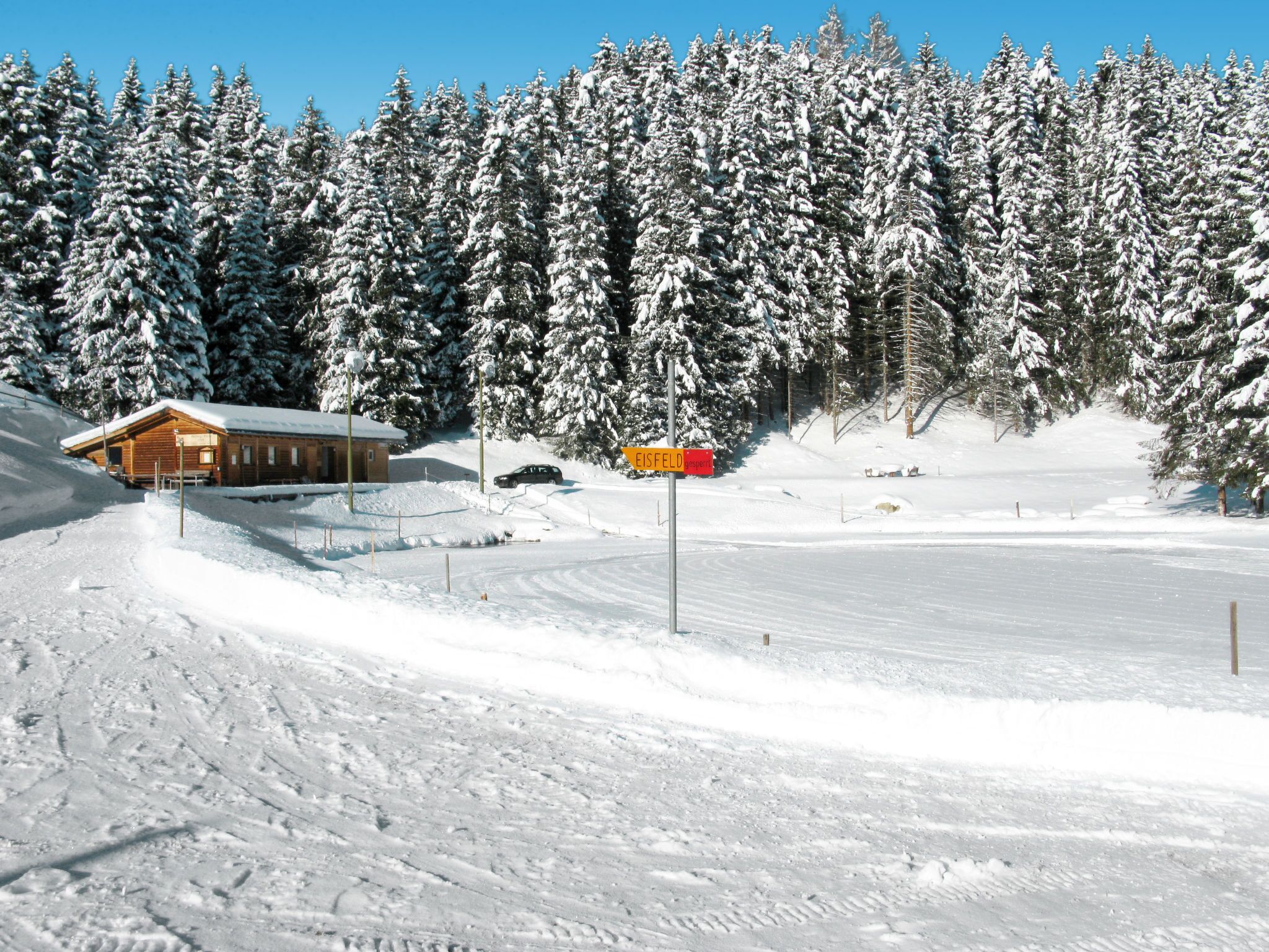 Un paysage enneigé avec un chalet, un panneau indicateur et une piste de ski.