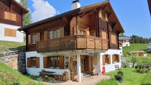 A two-story wooden house with a balcony, stone foundation, and a garden. - Baria Sut 5, (Oberurmein), by Interhome (Urmein)