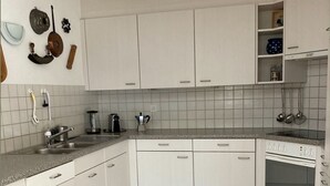 A kitchen with white cabinets, a tiled backsplash, a built-in oven, and a countertop with various appliances. - Baria Sut 5, (Oberurmein), by Interhome (Urmein)