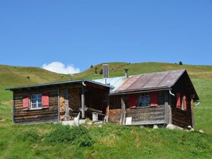Een rustieke houten hut met een metalen dak, gelegen op een grasheuvel onder een heldere lucht.