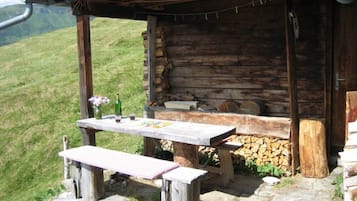 Una cabana de fusta rústica amb una banca de pedra i taula de pícnic, envoltada per una vessant de prada.