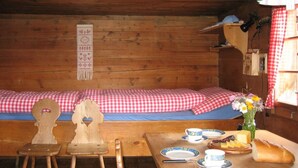 L’intérieur d’un chalet en bois, avec un lit, deux chaises, une table avec des assiettes et des tasses, un vase rempli de fleurs et une étagère avec une lampe.