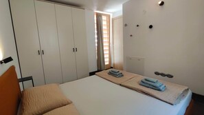 Ein Schlafzimmer mit einem Bett, einem Kleiderschrank, einem Fenster mit Vorhängen und einer Wand mit Lichtschaltern.