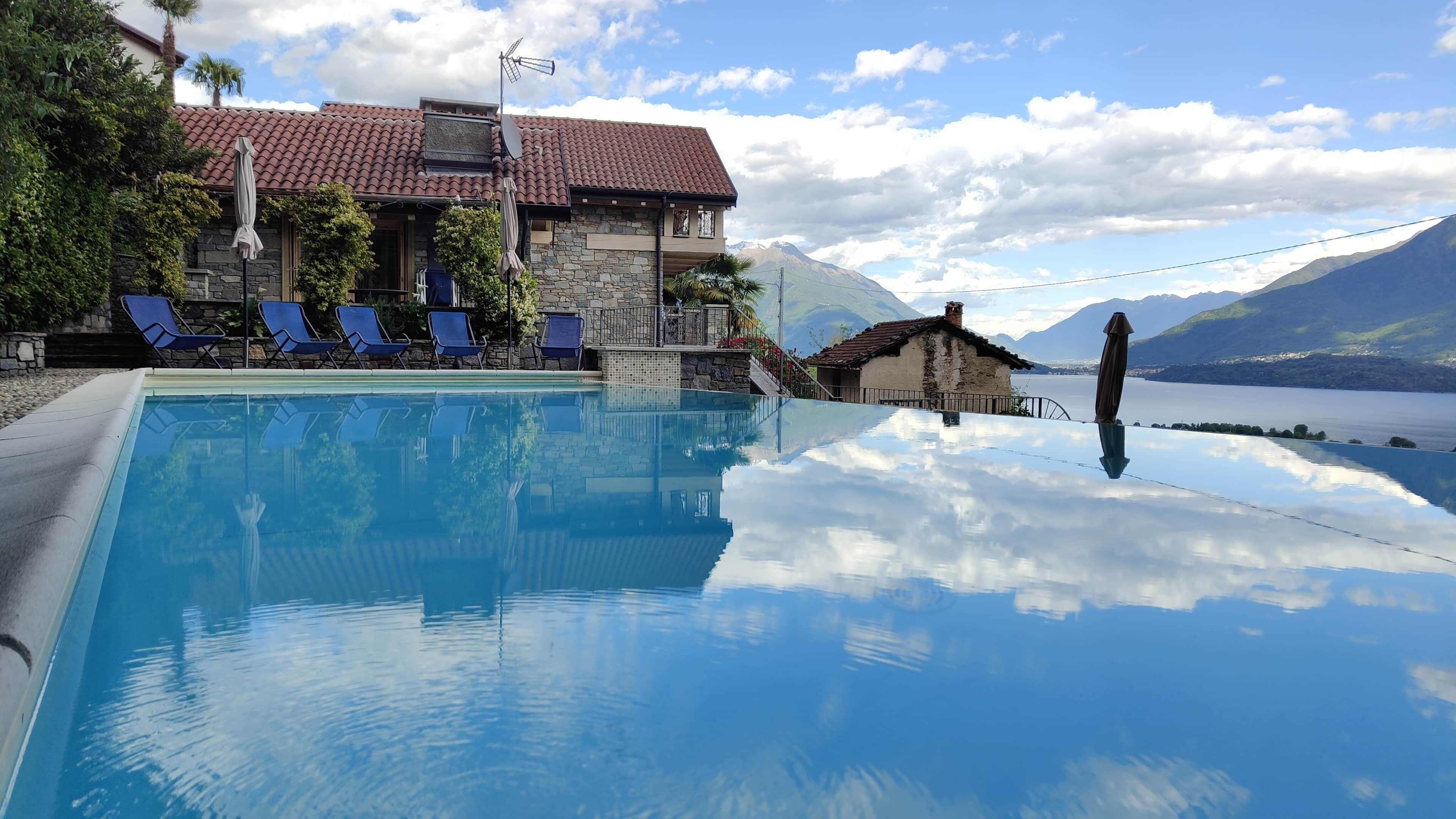 A swimming pool with clear water, a stone building with a tiled roof, and a mountain view.