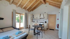 Ein Schlafzimmer mit einem Bett, einem kleinen Esstisch mit Stühlen, einer Küchenzeile mit Schränken und einer Holzbalkendecke.