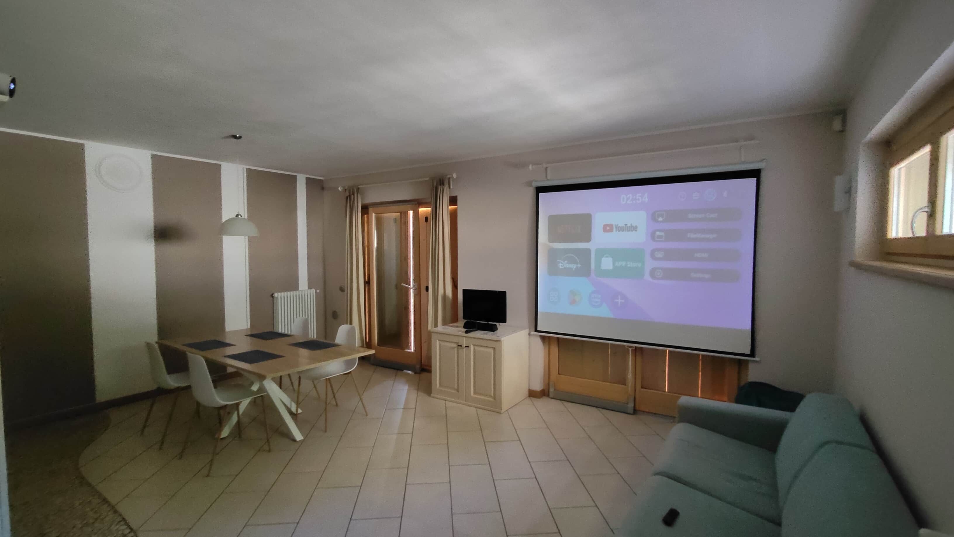 A living room with a TV screen displaying a YouTube interface, a dining area with a table and chairs, and a sofa.