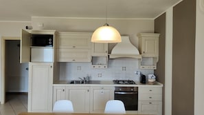 Eine moderne Küche mit Gasherd, Backofen und integriertem Mikrowellenherd. Weiße Schränke, eine Pendelleuchte und eine Fliesenrückwand.