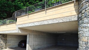 A stone building with a covered parking area and a metal railing on the upper level. - Apartments Chalet al Lac - Flowers - Pool & Lake Como View (San Gregorio)