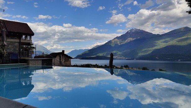 En pool der spejler himlen og bjergene, en bygning i sten, samt udsigt til en sø og bjerge.