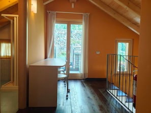 Ein Zimmer mit Holzboden, einem Tisch mit Stühlen, einem Fenster mit Vorhängen und einer Treppe mit Geländer.