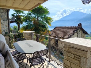 Una terraza con mesa y sillas, paredes de piedra y vistas a una montaña y un lago.