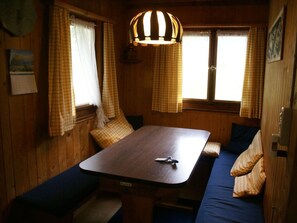 Interior de una cabaña con una mesa de madera, asientos tipo banco y una lámpara colgante.