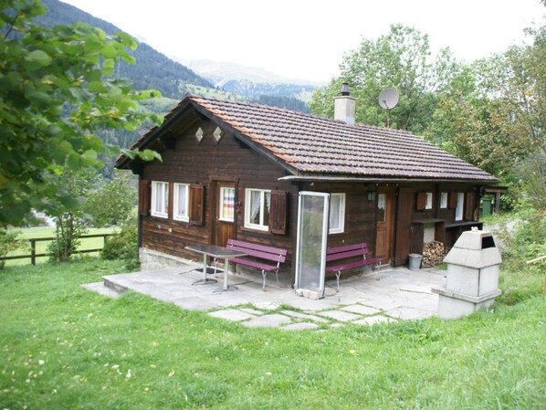 A wooden cabin with a tiled roof, a bench, and a fireplace.