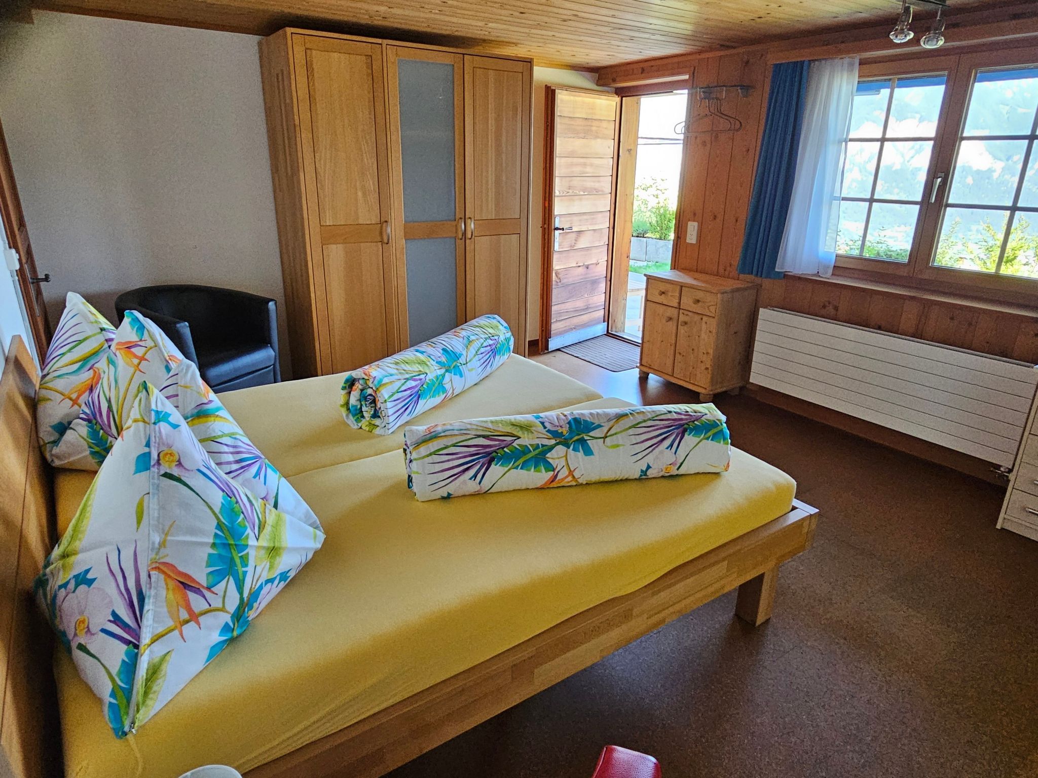 Een kamer met een bed, een stoel, een houten kledingkast en een raam met uitzicht.