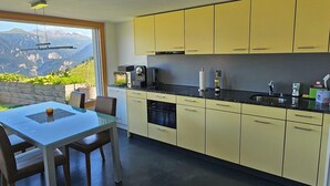 Una cocina moderna con armarios amarillos, una mesa de comedor con sillas y vistas a montañas a través de amplios ventanales.