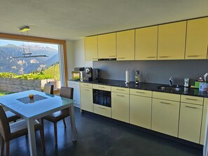 Eine moderne Küche mit gelben Schränken, einem Esstisch mit Stühlen und Blick auf Berge durch große Fenster.